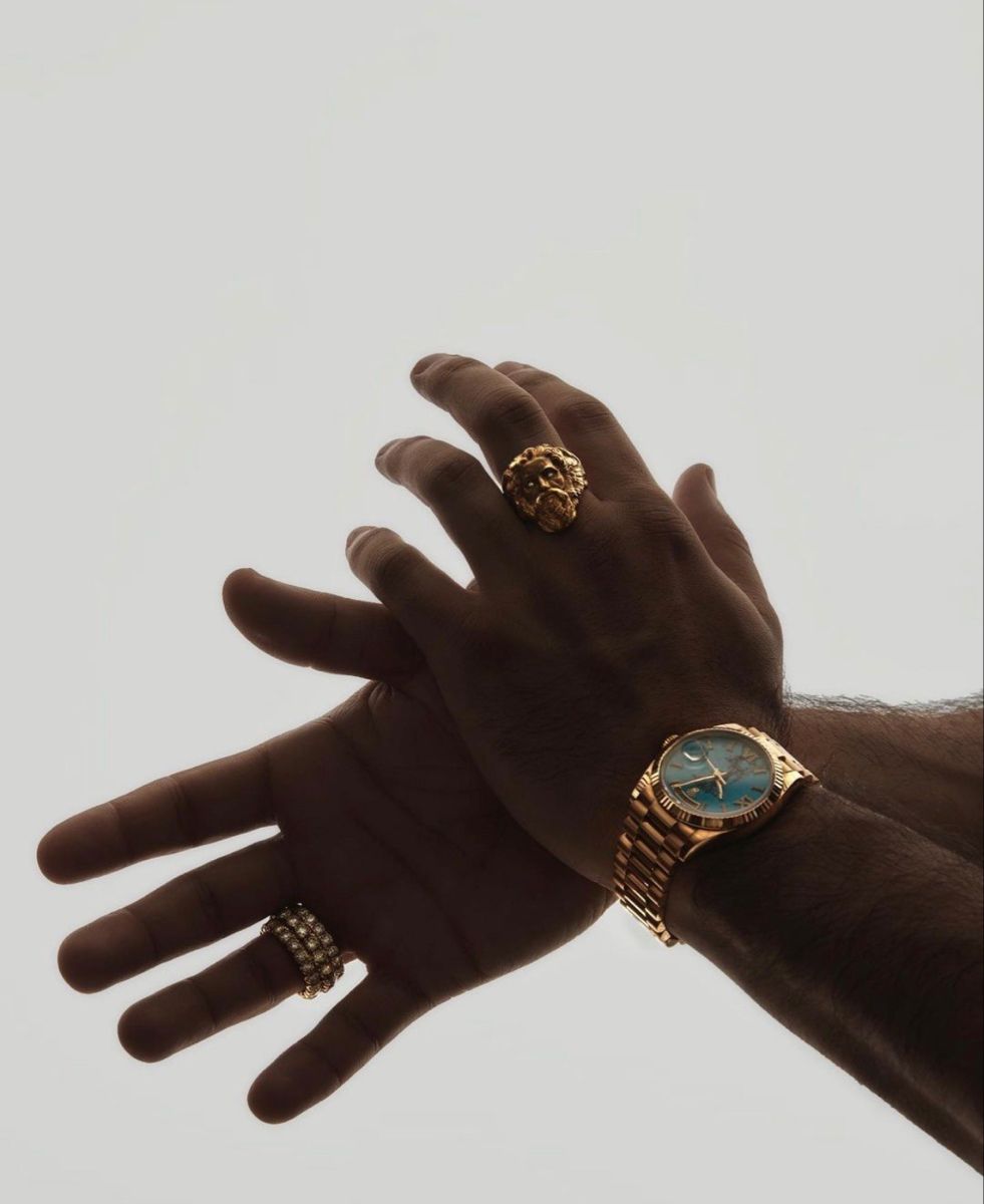 Crossed hands wearing a gold watch against a pale sky