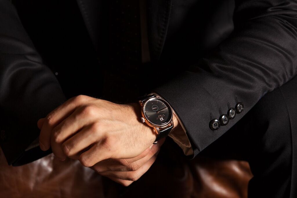 A black-dial watch under a dark suit cuff